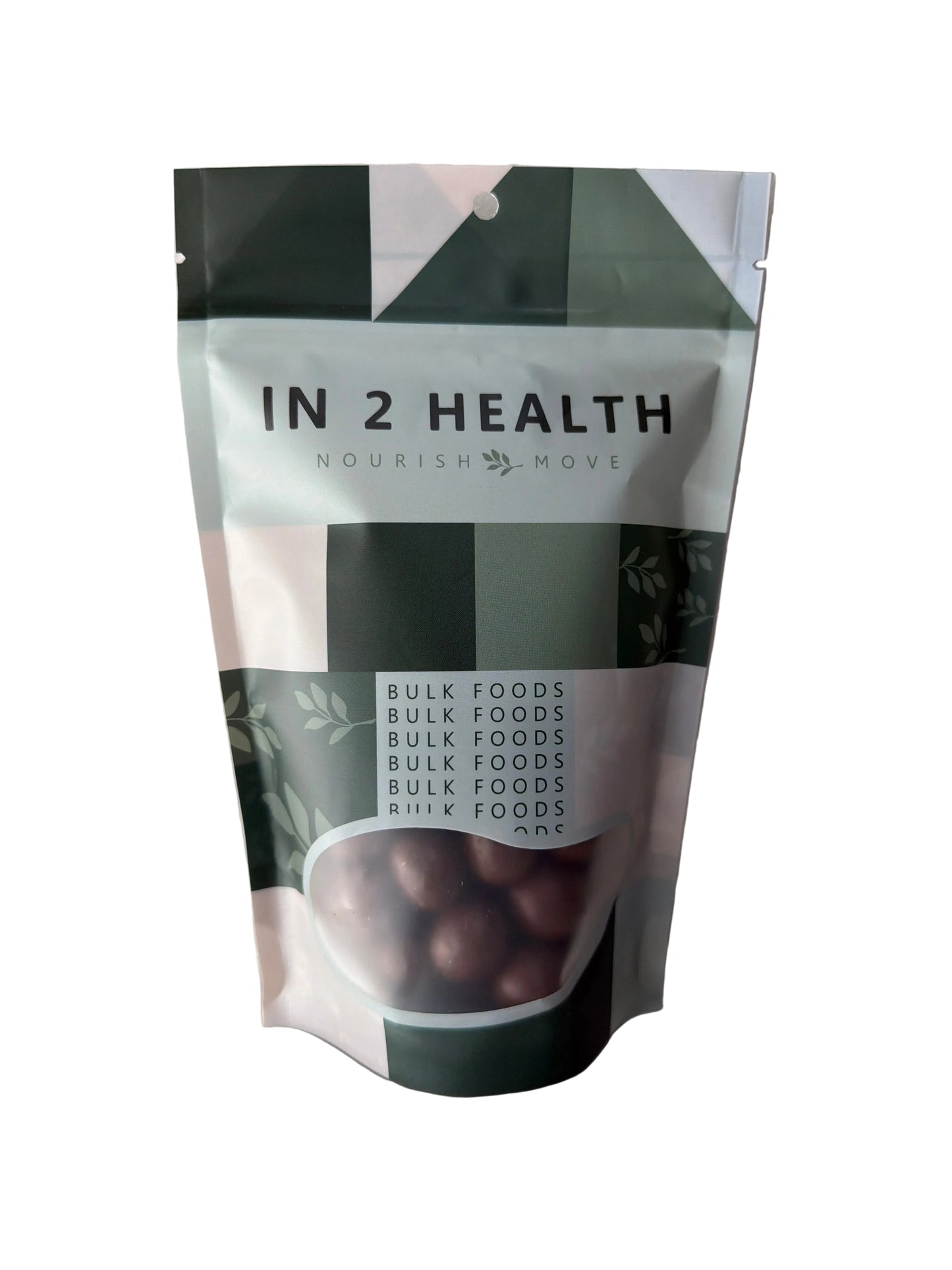 A stand-up pouch of IN 2 HEALTH Nourish Ready bulk food, featuring a white and dark green geometric design with a clear window showing dark brown bulk food inside, photographed on a white surface.