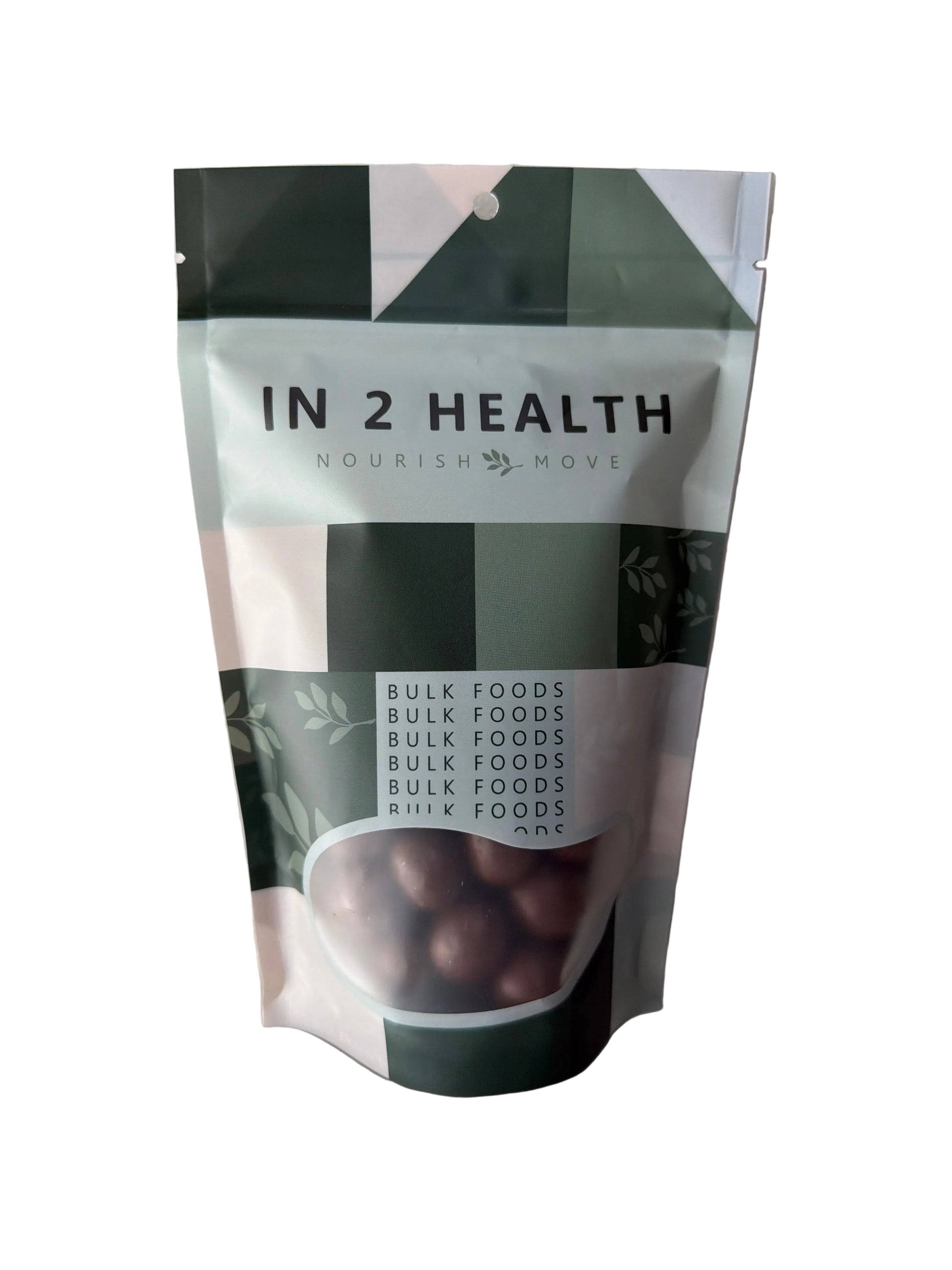 A stand-up pouch of IN 2 HEALTH Nourish Ready bulk food, featuring a white and dark green geometric design with a clear window showing dark brown bulk food inside, photographed on a white surface.